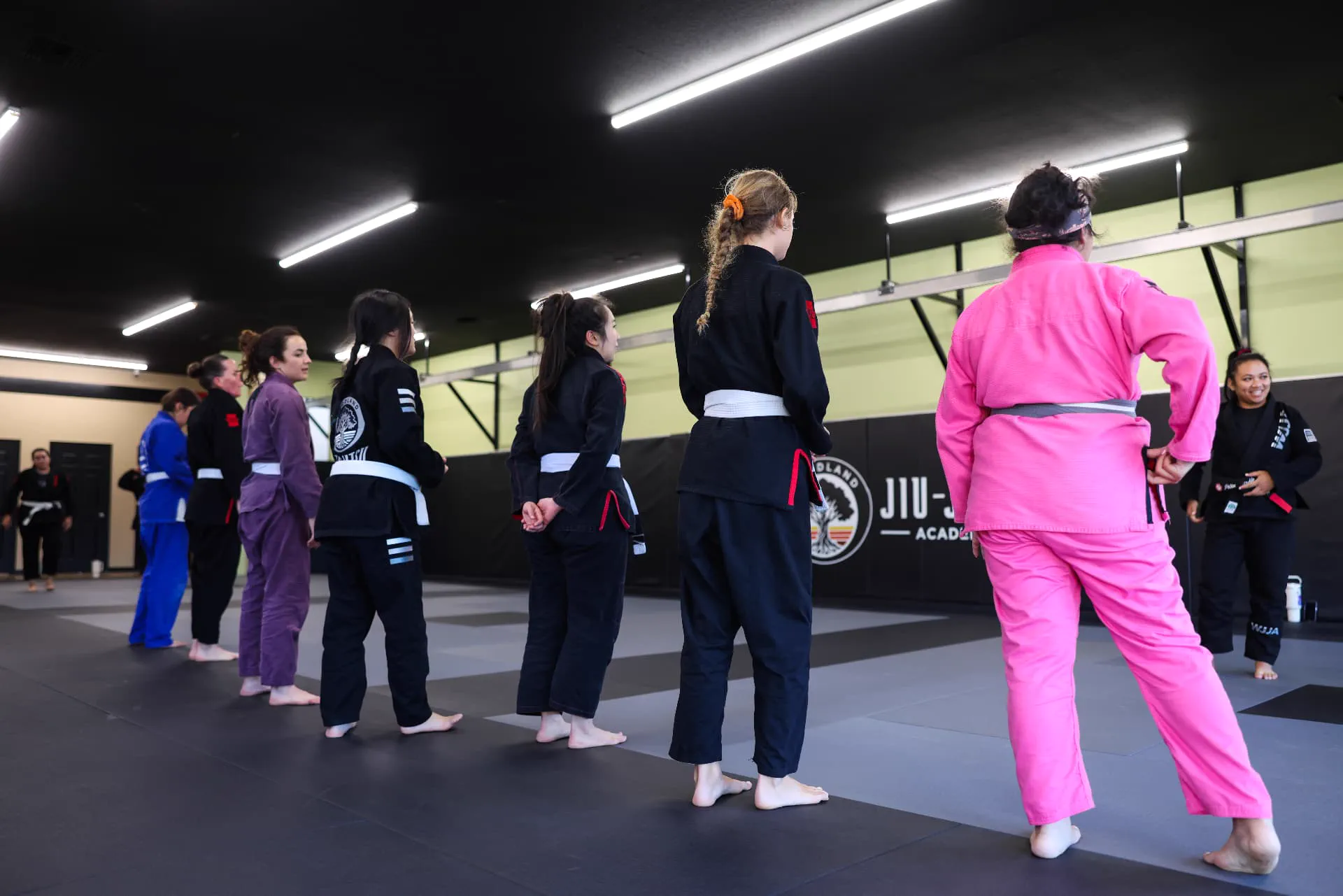 Women in gis lined up across the mat facing their instructor during a women's Jiu-Jitsu class