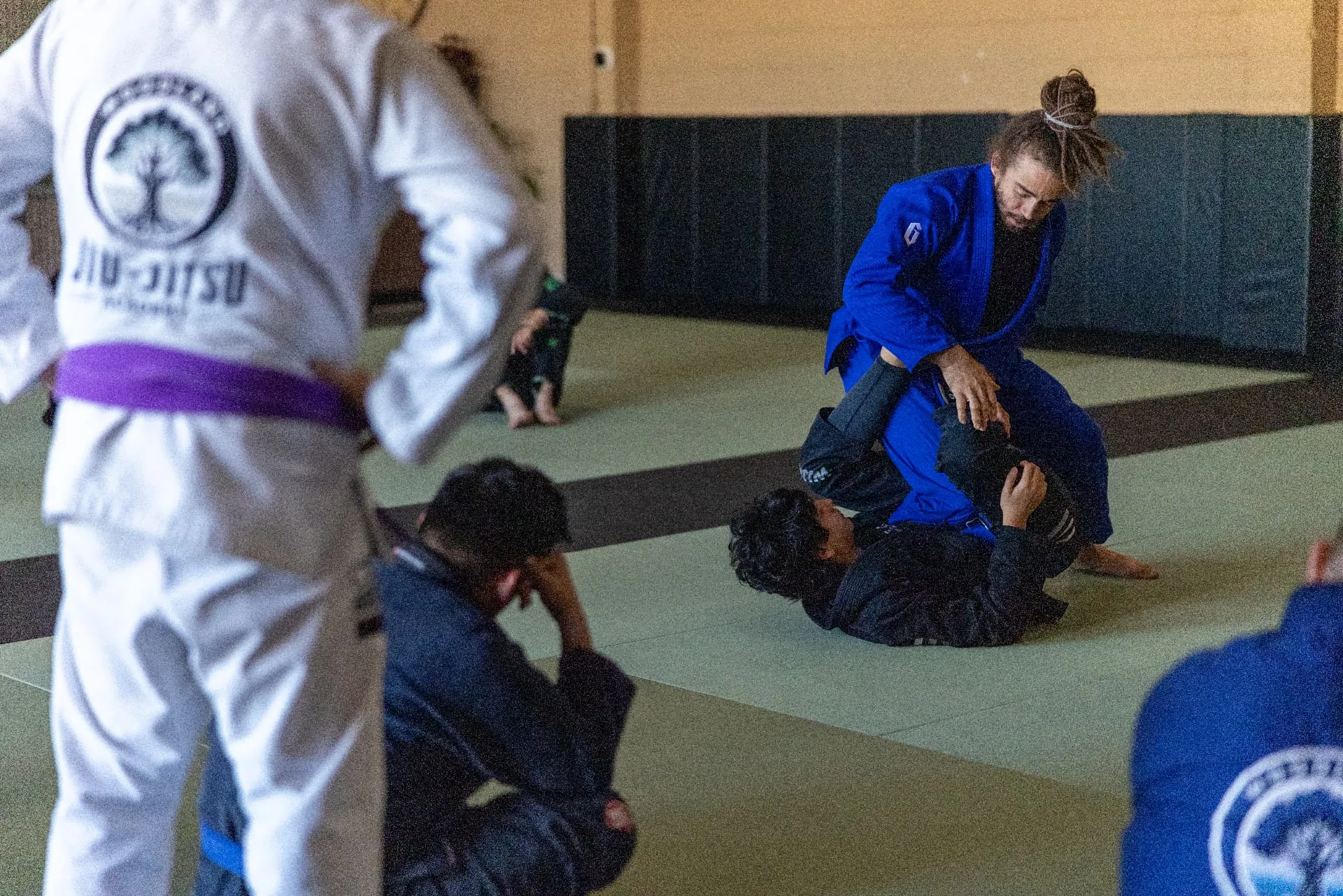 An instructor demonstrating a guard pass on the mat while students in gis watch closely