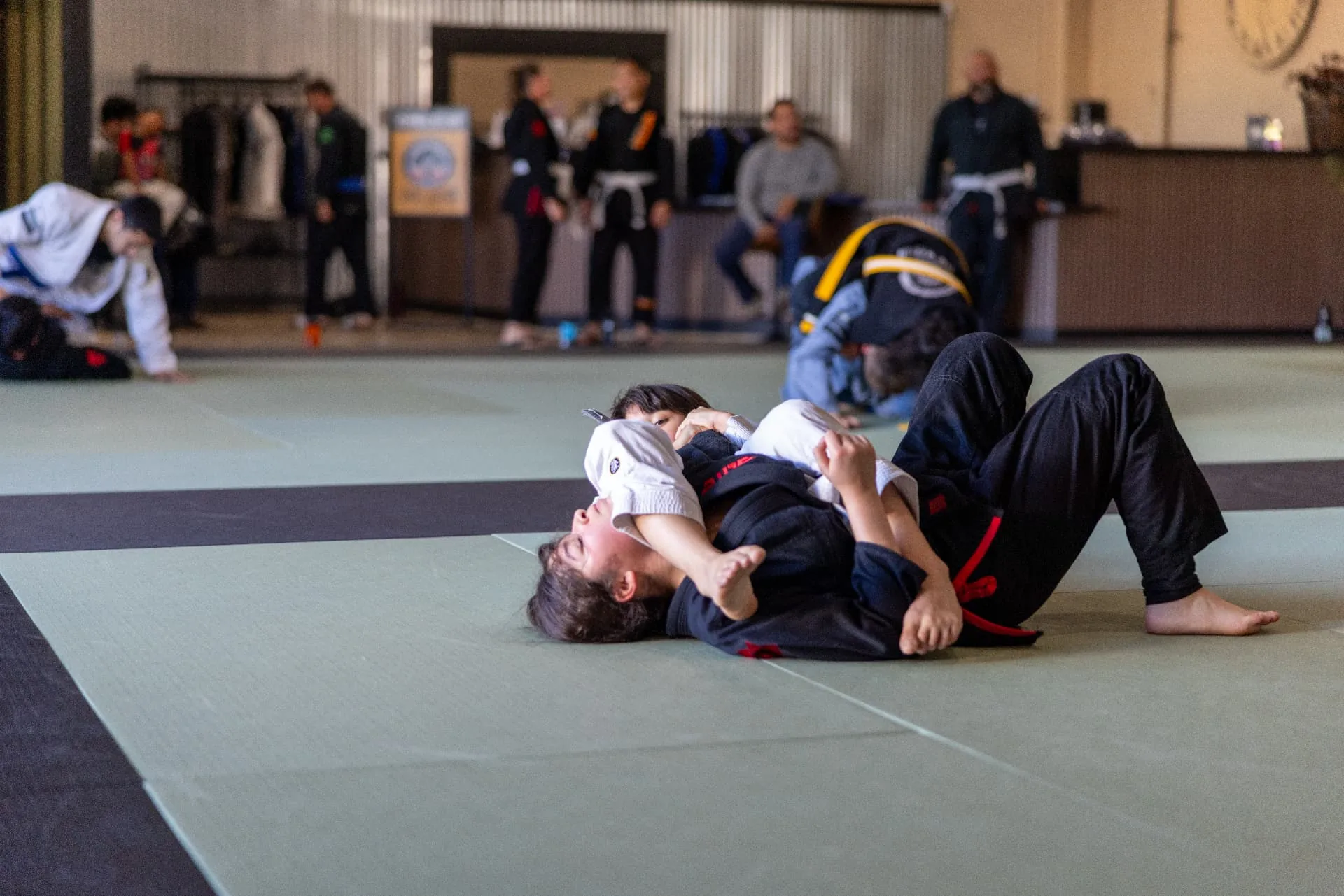 A young student practicing a guard position with a coach during kids Jiu-Jitsu class
